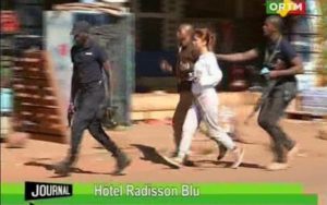 In this TV image taken from Mali TV ORTM, a woman is led away by security personnel from the Radisson Blu Hotel hotel in Bamako, Mali, Friday Nov. 20, 2015. Men shouting "God is great" and armed with guns and throwing grenades stormed into the Radisson Blu Hotel in Mali's capital Friday morning. (Mali TV ORTM, AP) MALI OUT