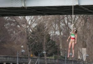 A Femen activist, Sarah Constantin, is hanged from a noose-like rope from a Paris bridge to call attention to the large number of executions in Iran as she stages a protest against visiting Iranian President Hassan Rouhani in Paris, Thursday, Jan. 28, 2016. A near-naked woman hanging from a noose-like rope from a Paris bridge has sent a message to visiting Iranian President Hassan Rouhani. (ANSA/AP Photo/Zacharie Scheurer)